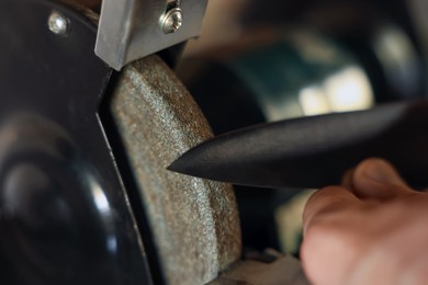 Photo of Man sharpening knife with bench grinder indoors, closeup