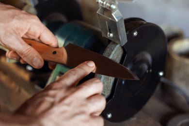Photo of Man sharpening knife with bench grinder indoors, closeup