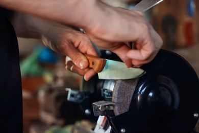 Photo of Man sharpening knife with bench grinder indoors, closeup
