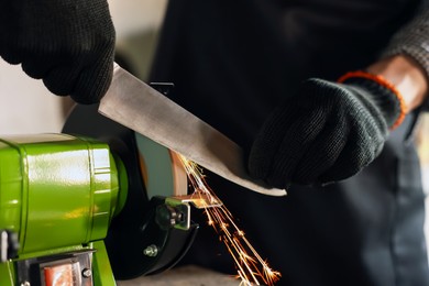 Photo of Man sharpening knife with bench grinder indoors, closeup