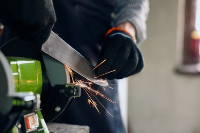 Photo of Man sharpening knife with bench grinder indoors, closeup