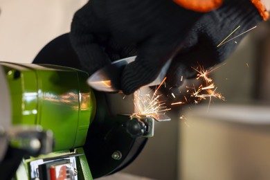 Photo of Man sharpening knife with bench grinder indoors, closeup