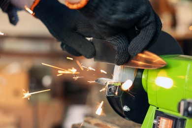 Photo of Man sharpening knife with bench grinder indoors, closeup