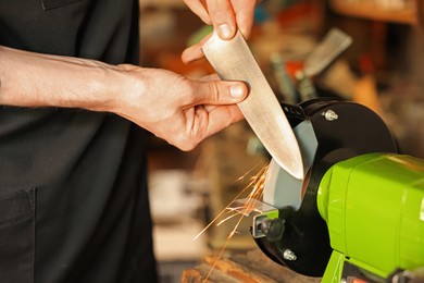 Photo of Man sharpening knife with bench grinder indoors, closeup