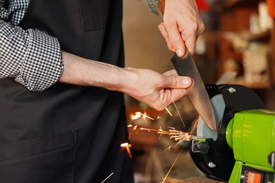 Photo of Man sharpening knife with bench grinder indoors, closeup