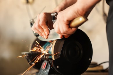 Photo of Man sharpening knife with bench grinder indoors, closeup