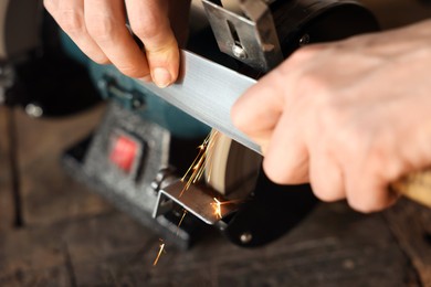 Photo of Man sharpening knife with bench grinder indoors, closeup