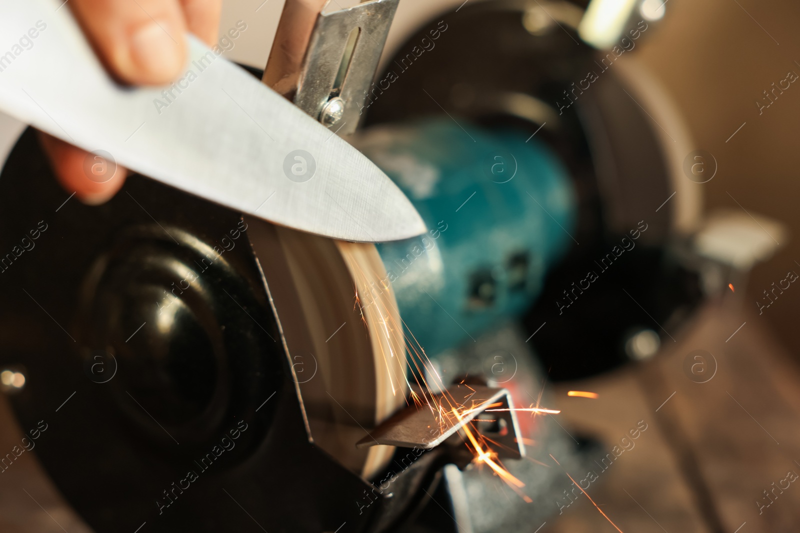 Man sharpening knife with bench grinder indoors, closeup Photo of Man sharpening knife with bench grinder indoors, closeup