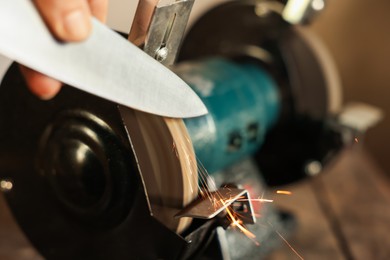 Photo of Man sharpening knife with bench grinder indoors, closeup