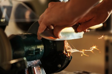 Photo of Man sharpening knife with bench grinder indoors, closeup