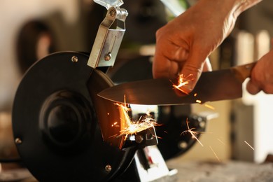 Photo of Man sharpening knife with bench grinder indoors, closeup