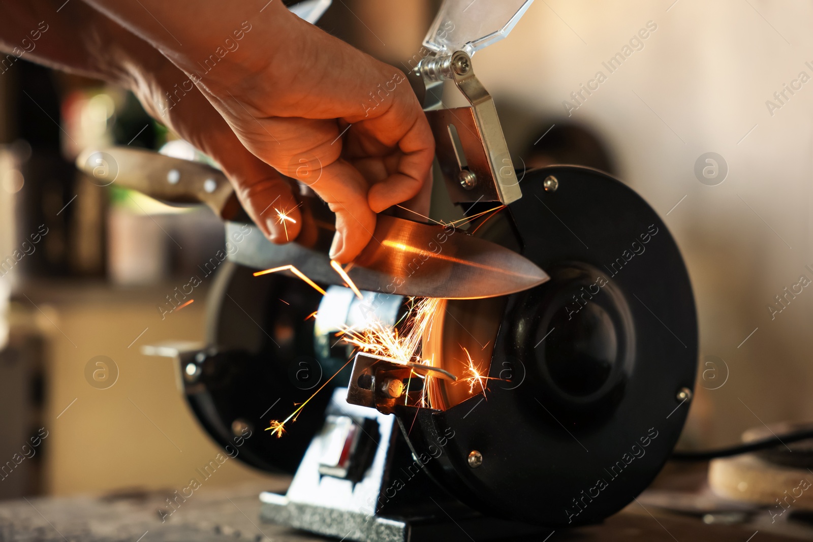 Man sharpening knife with bench grinder indoors, closeup Photo of Man sharpening knife with bench grinder indoors, closeup
