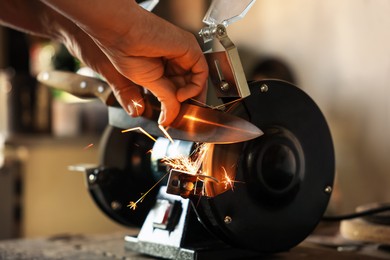 Photo of Man sharpening knife with bench grinder indoors, closeup