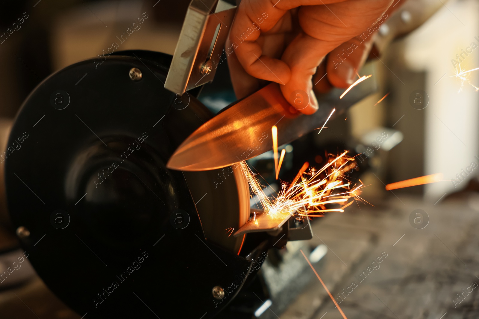 Man sharpening knife with bench grinder indoors, closeup Photo of Man sharpening knife with bench grinder indoors, closeup