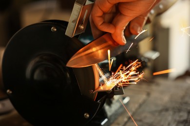 Photo of Man sharpening knife with bench grinder indoors, closeup