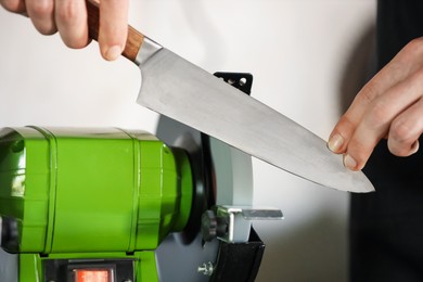 Photo of Man sharpening knife with bench grinder indoors, closeup
