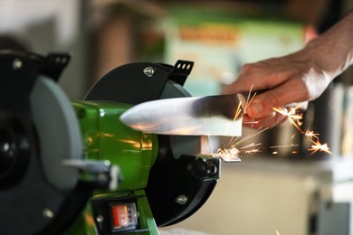 Photo of Man sharpening knife with bench grinder indoors, closeup