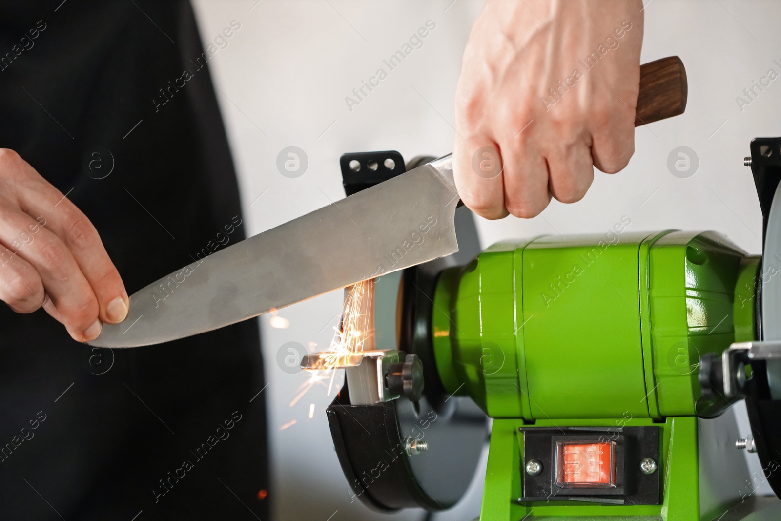 Man sharpening knife with bench grinder indoors, closeup Photo of Man sharpening knife with bench grinder indoors, closeup