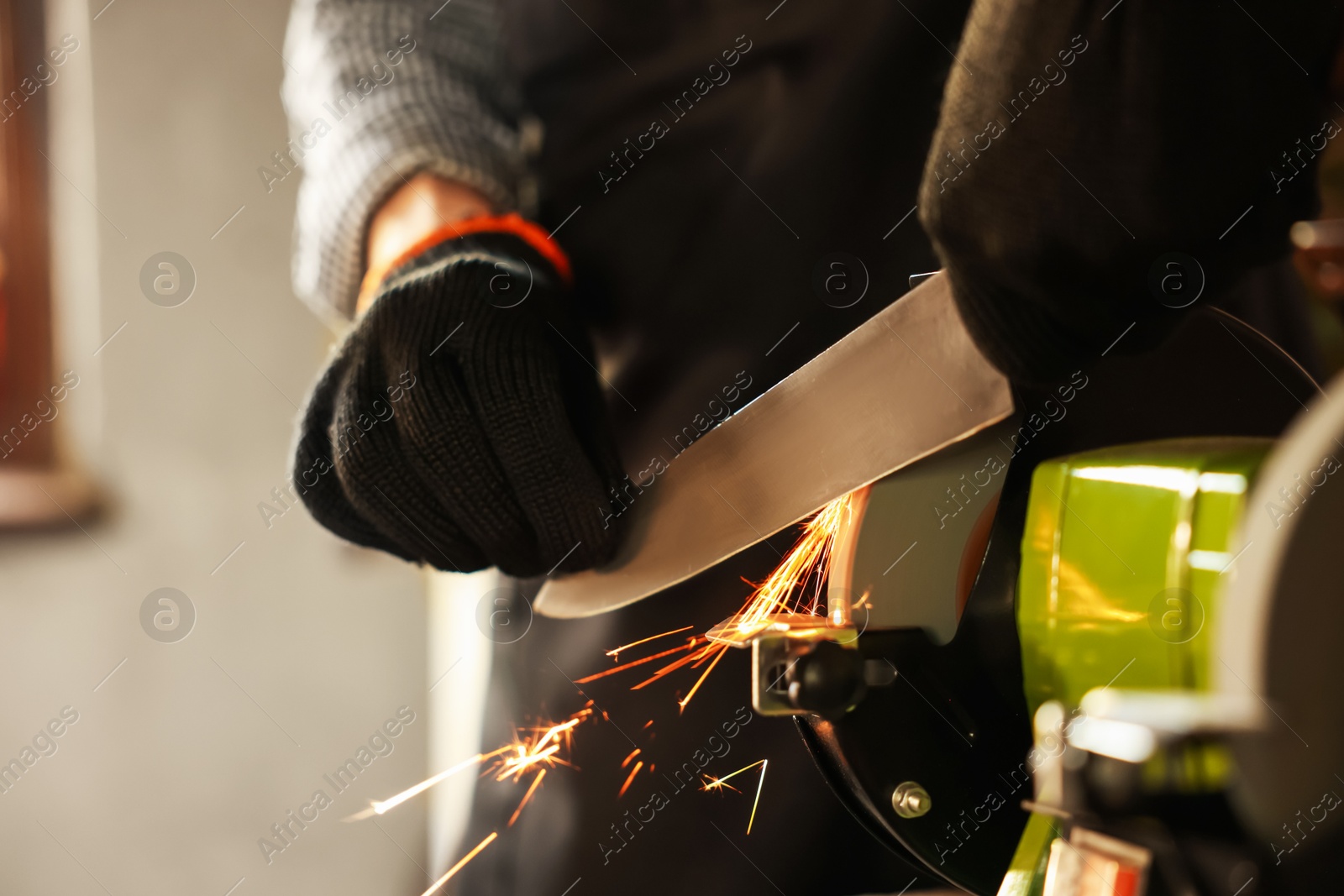 Man sharpening knife with bench grinder indoors, closeup Photo of Man sharpening knife with bench grinder indoors, closeup