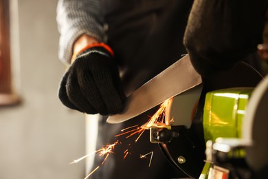 Photo of Man sharpening knife with bench grinder indoors, closeup