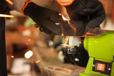 Photo of Man sharpening knife with bench grinder indoors, closeup