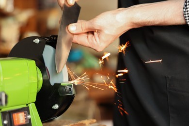 Photo of Man sharpening knife with bench grinder indoors, closeup
