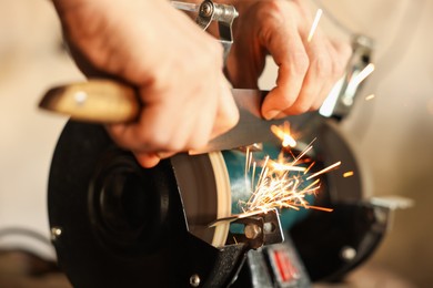 Photo of Man sharpening knife with bench grinder indoors, closeup
