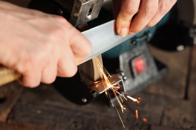 Photo of Man sharpening knife with bench grinder indoors, closeup