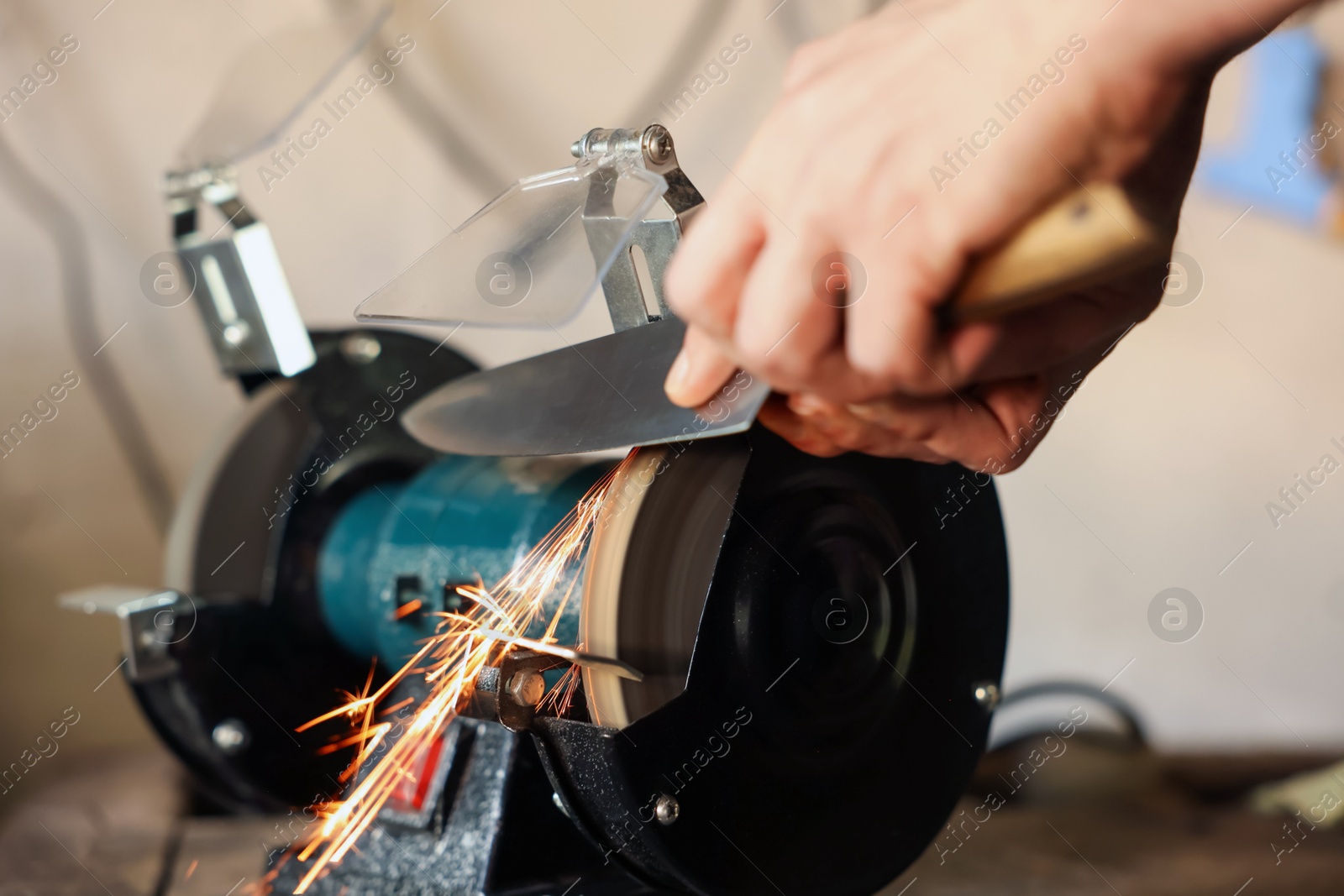 Man sharpening knife with bench grinder indoors, closeup Photo of Man sharpening knife with bench grinder indoors, closeup