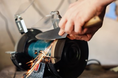Photo of Man sharpening knife with bench grinder indoors, closeup