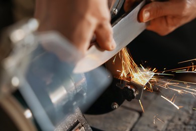 Photo of Man sharpening knife with bench grinder indoors, closeup