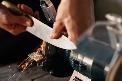 Photo of Man sharpening knife with bench grinder indoors, closeup