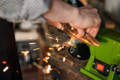 Photo of Man sharpening knife with bench grinder indoors, closeup