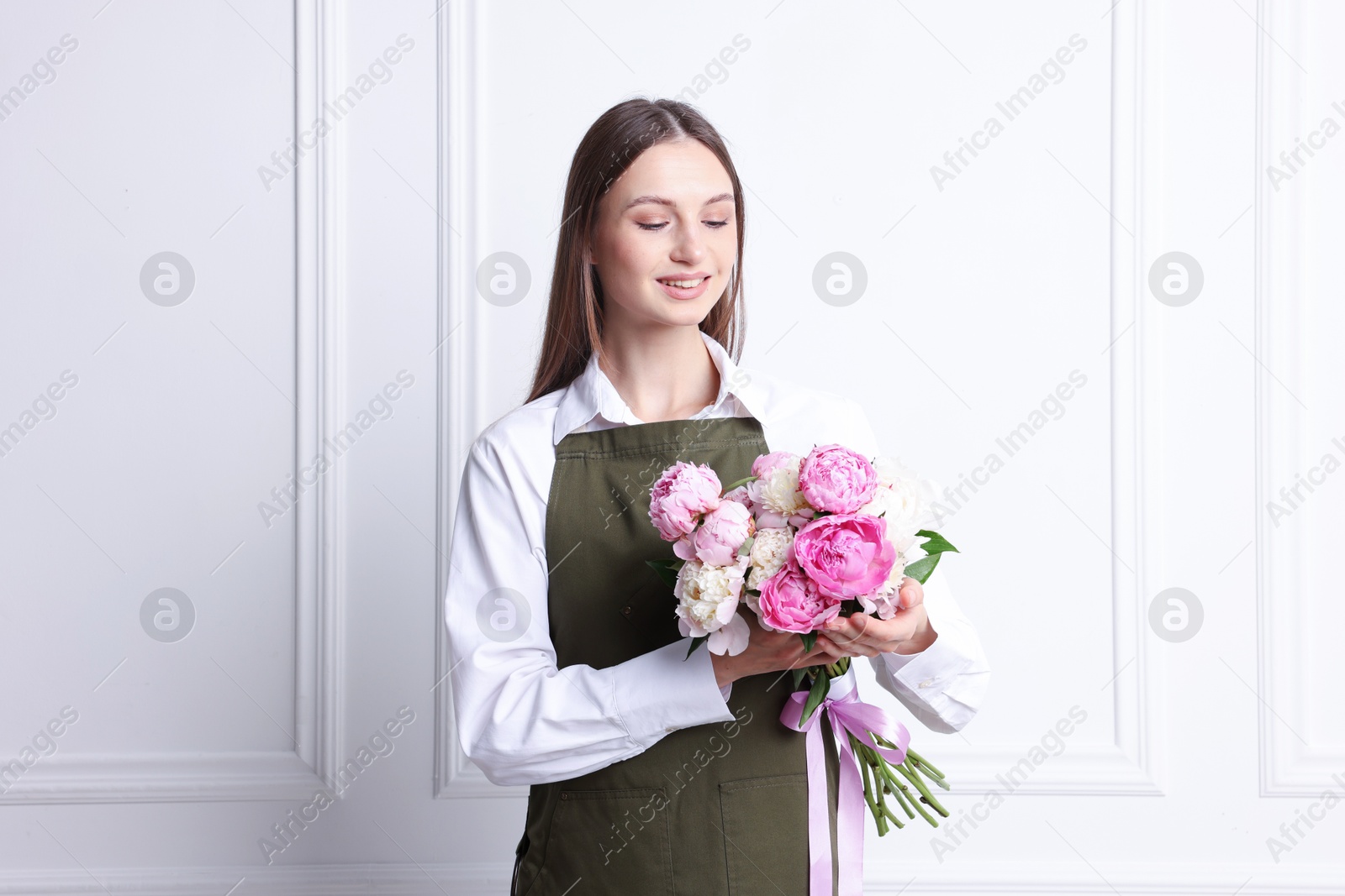 Florist with beautiful bouquet of peonies near white wall indoors Photo of Florist with beautiful bouquet of peonies near white wall indoors