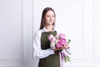 Photo of Florist with beautiful bouquet of peonies near white wall indoors