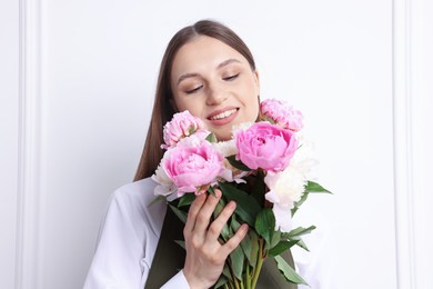 Photo of Florist with beautiful bouquet of peonies near white wall indoors