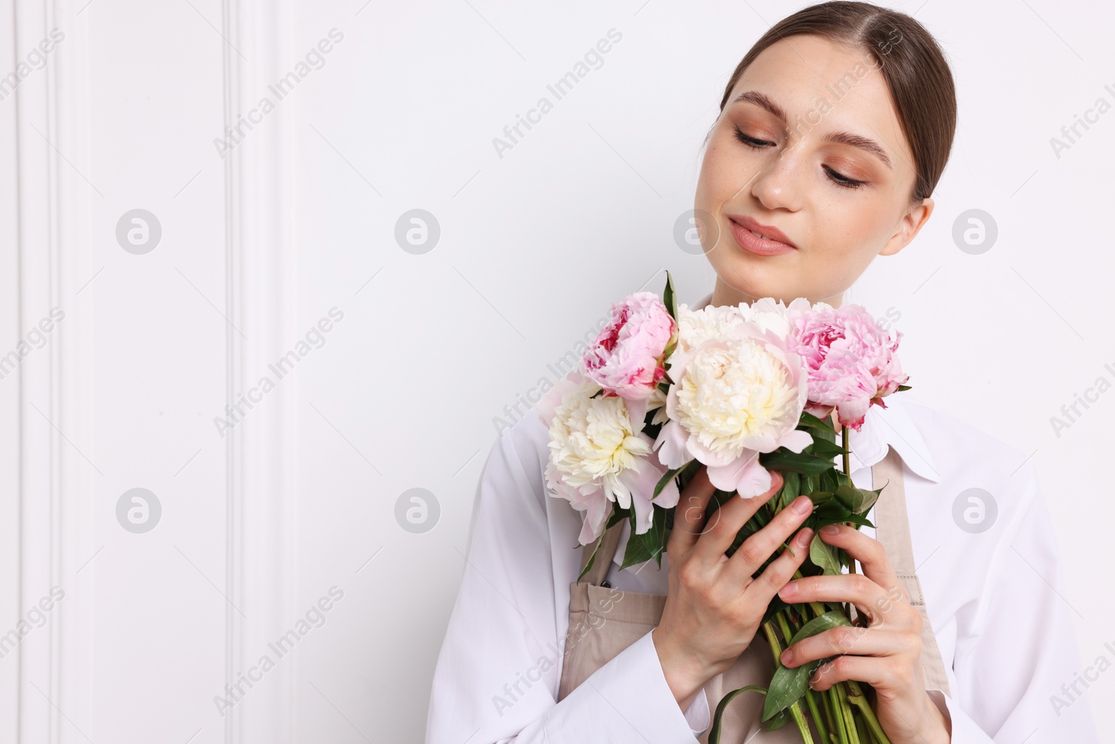 Florist with beautiful bouquet of peonies near white wall indoors, space for text Photo of Florist with beautiful bouquet of peonies near white wall indoors, space for text