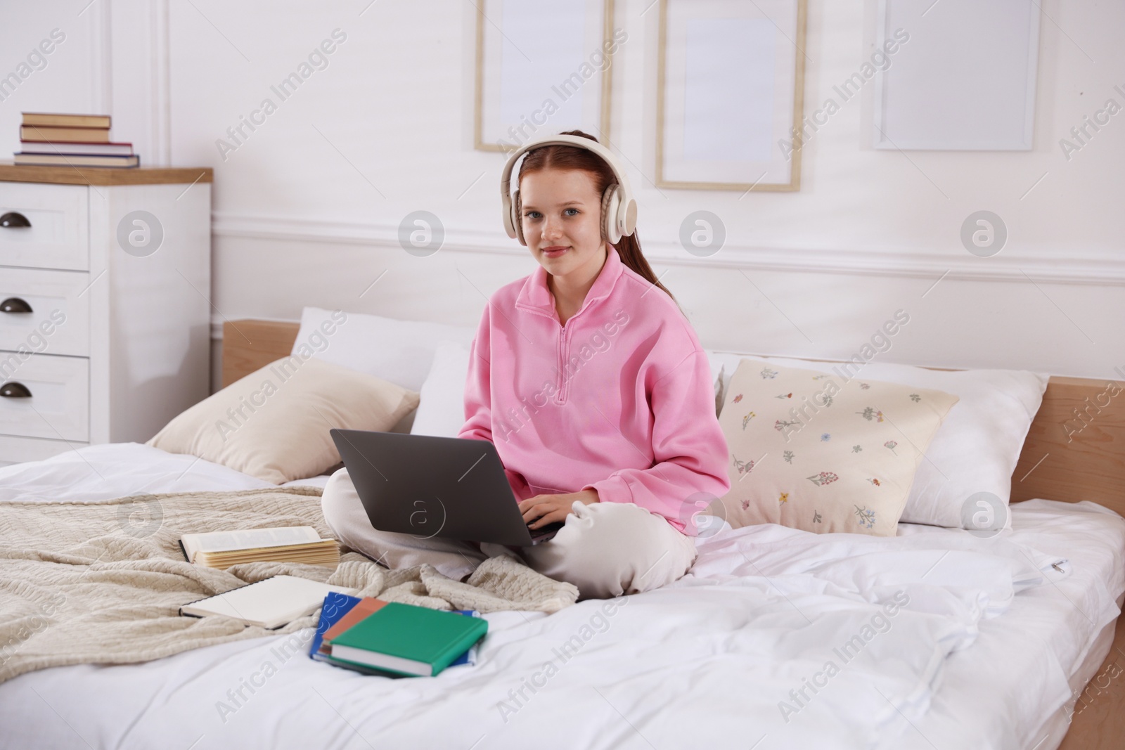Teenage student in headphones using laptop while studying on bed at home Photo of Teenage student in headphones using laptop while studying on bed at home