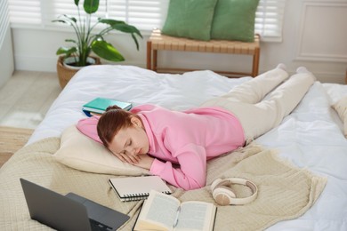 Photo of Tired teenage student sleeping near books and laptop on bed at home