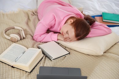 Photo of Tired teenage student sleeping near books and laptop on bed at home, above view