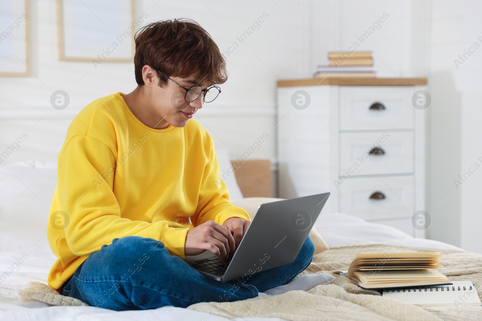 Teenage student in glasses using laptop while studying on bed at home Photo of Teenage student in glasses using laptop while studying on bed at home