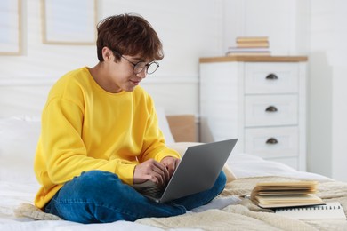 Photo of Teenage student in glasses using laptop while studying on bed at home