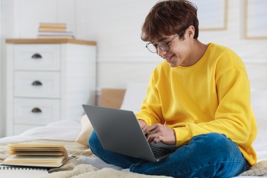 Photo of Teenage student in glasses using laptop while studying on bed at home