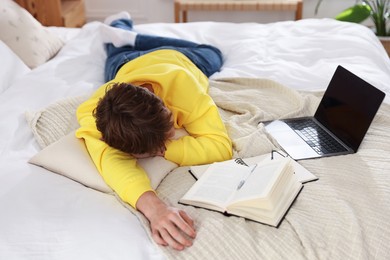Photo of Tired teenage student sleeping near books and laptop on bed at home