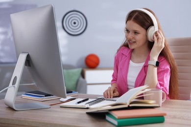 Photo of Teenage student with headphones using computer while studying at table indoors