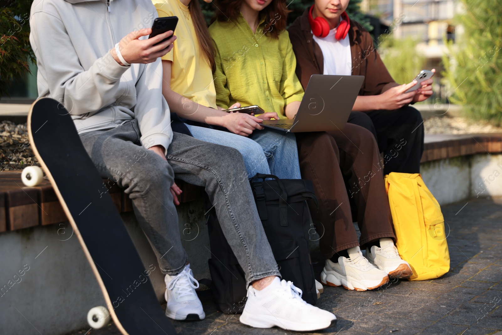 Teenagers with different devices on bench in park, closeup Photo of Teenagers with different devices on bench in park, closeup