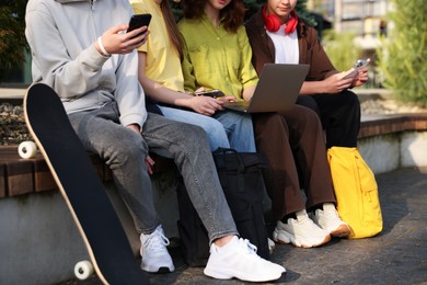 Photo of Teenagers with different devices on bench in park, closeup