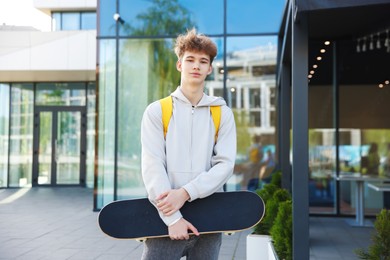 Photo of Teenage boy with skateboard and backpack near building outdoors