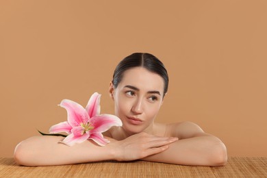 Photo of Beautiful woman after spa treatment with lily flower at bamboo table on beige background