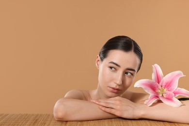 Photo of Beautiful woman after spa treatment with lily flower at bamboo table on beige background. Space for text